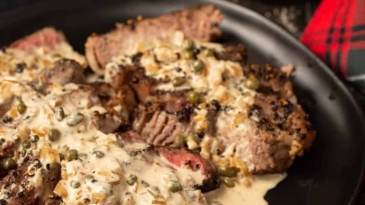 Steak au Poivre on a black platter with a bottle of Cognac.