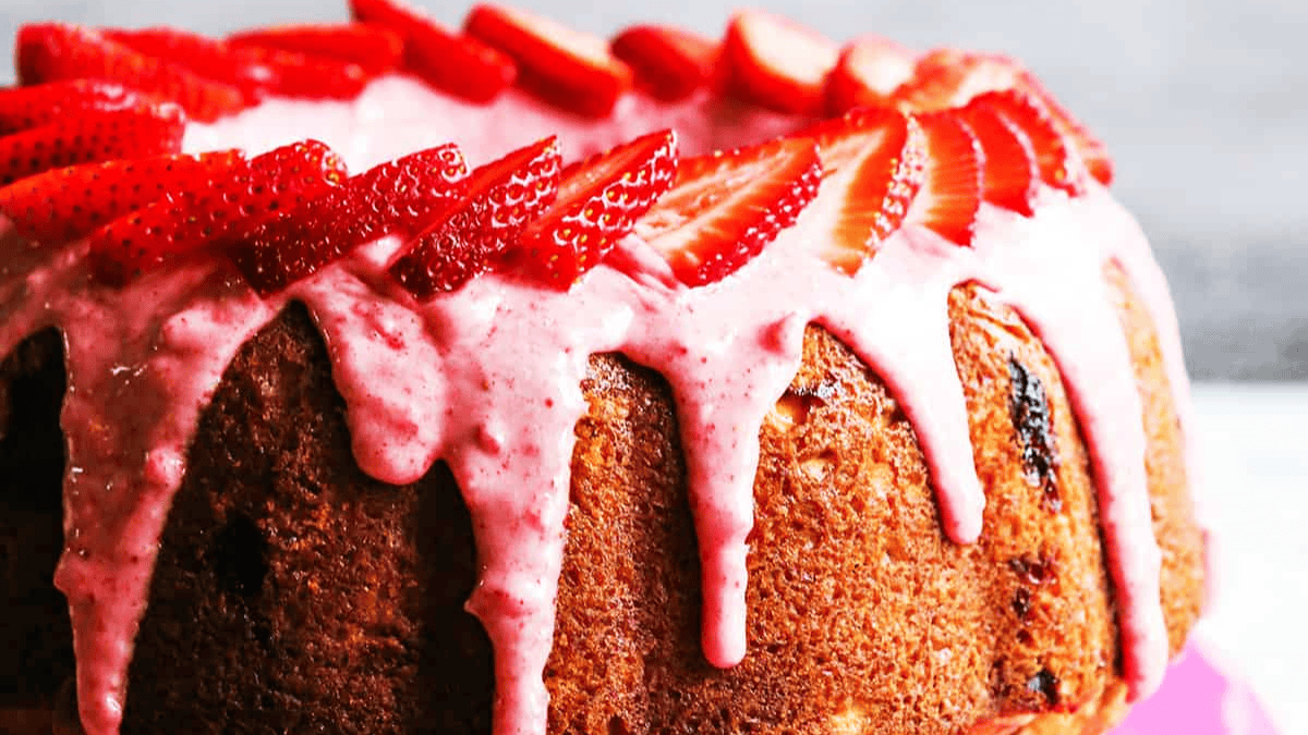 A close-up of an easy bundt cake topped with pink strawberry glaze dripping down the sides, garnished with fresh, sliced strawberries arranged in a circle.