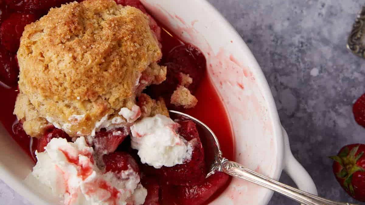 Strawberry cobbler in a white serving dish with whipped cream.