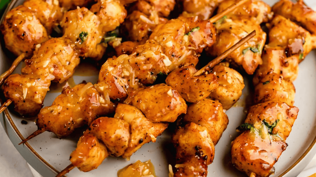 Grilled chicken skewers with a glossy, seasoned glaze are arranged on a white plate, showing juicy, golden-brown pieces of chicken threaded onto wooden sticks and garnished with herbs—perfect for fans of air fryer recipes.
