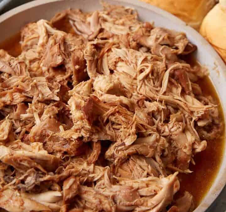 A platter of rolls next to pulled chicken.