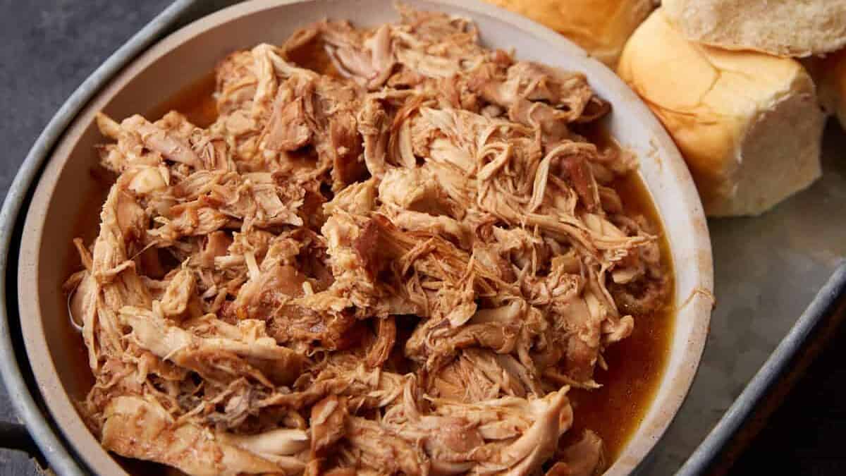 A platter of rolls next to pulled chicken.