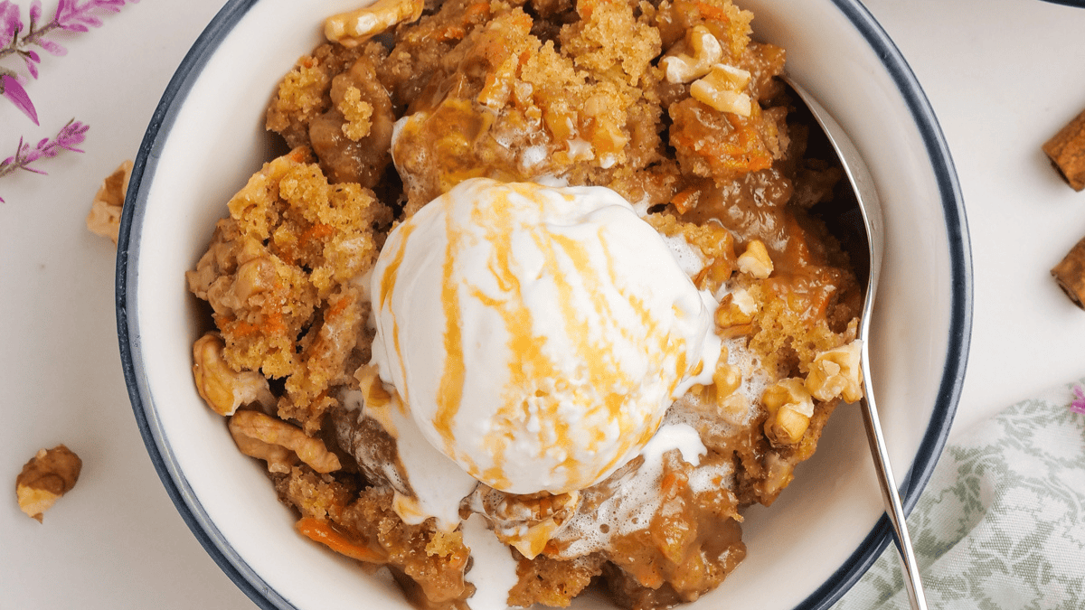 A bowl of warm apple crisp, a classic among old fashioned southern desserts, topped with vanilla ice cream and caramel sauce. Pieces of walnuts and crumbled topping are visible, with a spoon resting inside the bowl.