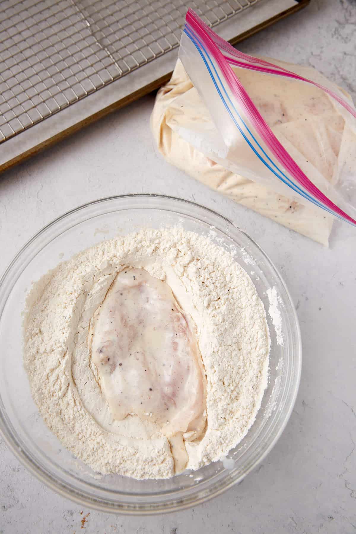 marinated chicken sitting inside of a glass bowl filled with flour mixture