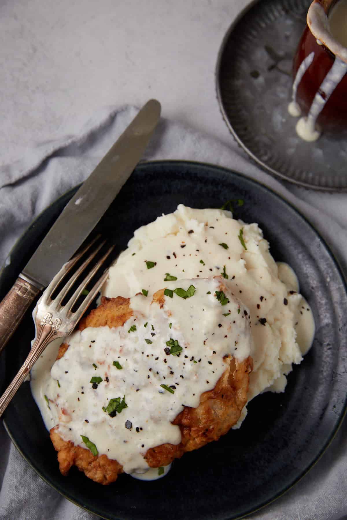 close up of chicken fried chicken with gravy on a black plate with a knife and fork