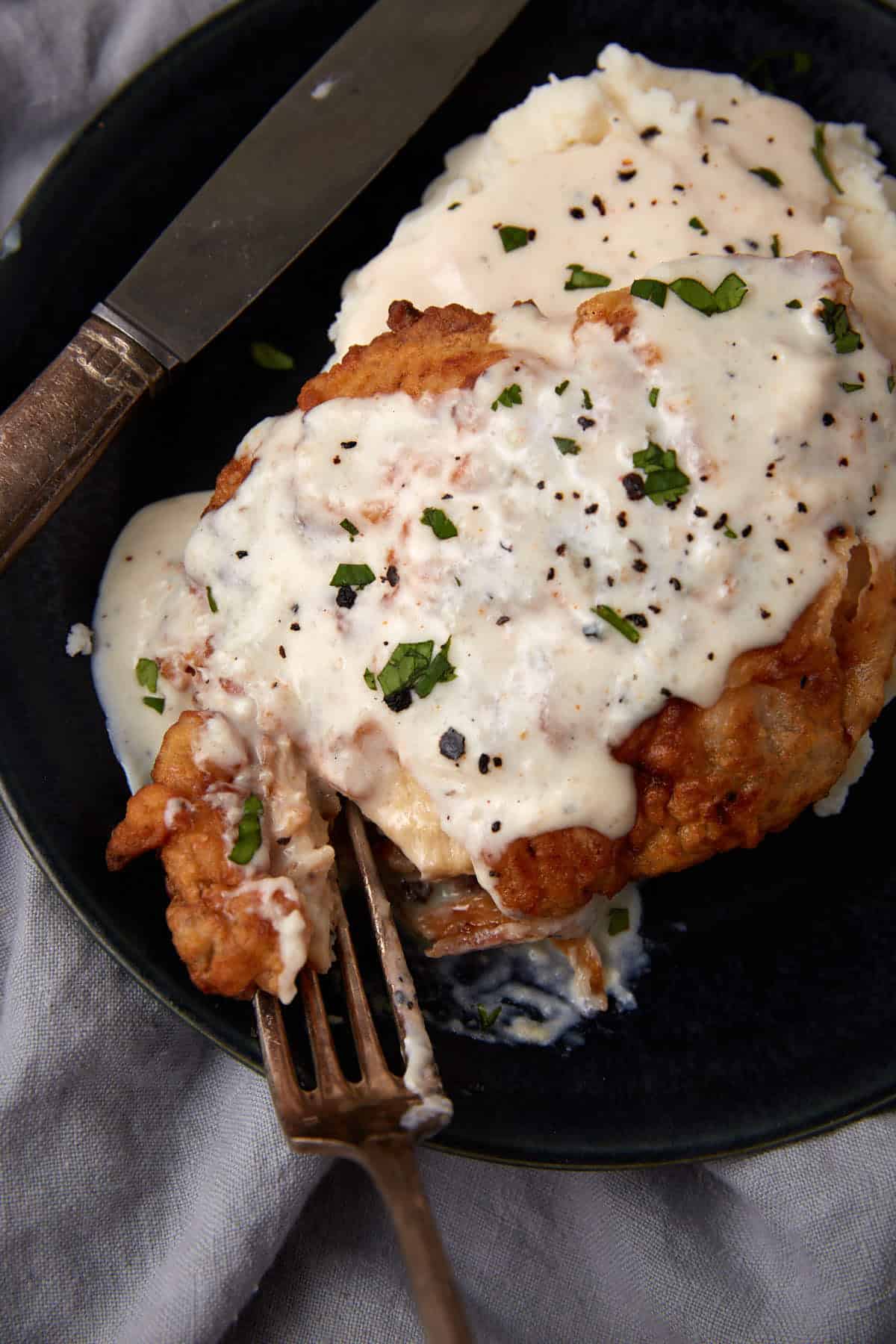 chicken fried chicken with gravy on a black plate being cut into with a fork
