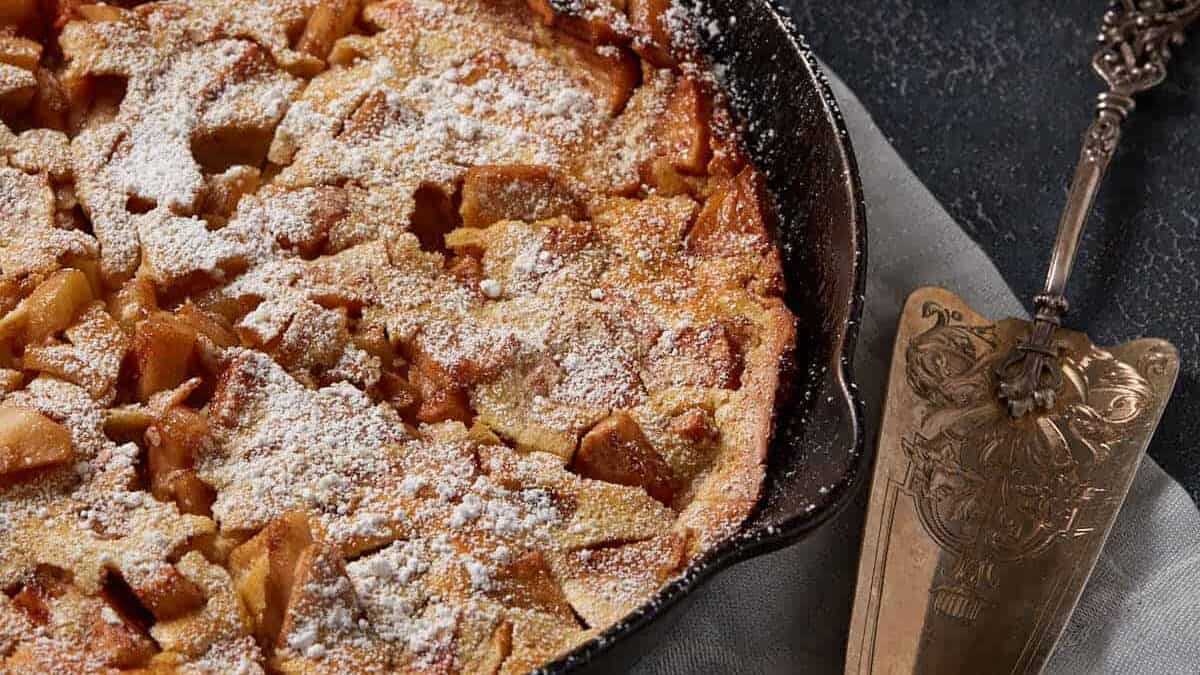 A Dutch baby pancake in a skillet next to a stack of plates.