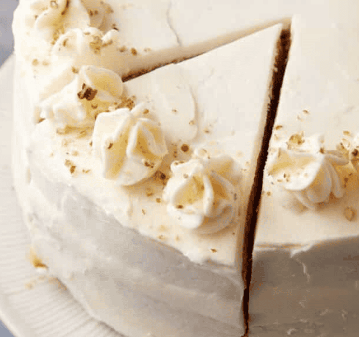 A round frosted cake with white icing and decorative swirls on top, one slice partially separated from the rest, displayed on a white plate—perfect inspiration for your next cake recipes.