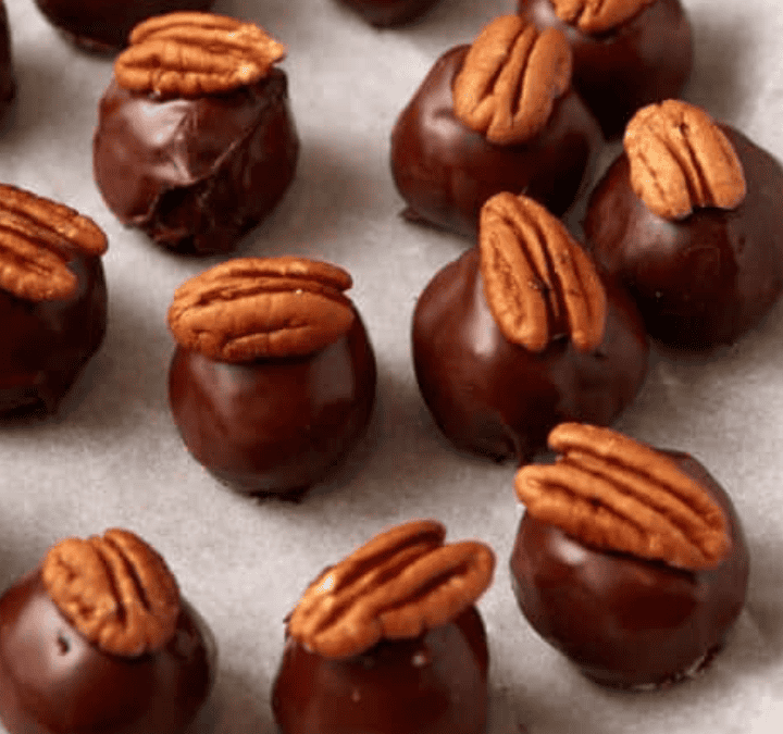 Rows of round chocolate truffles topped with pecan halves are arranged on parchment paper. With their glossy coating and decorative pecans, these treats make irresistible Super Bowl desserts for any celebration.