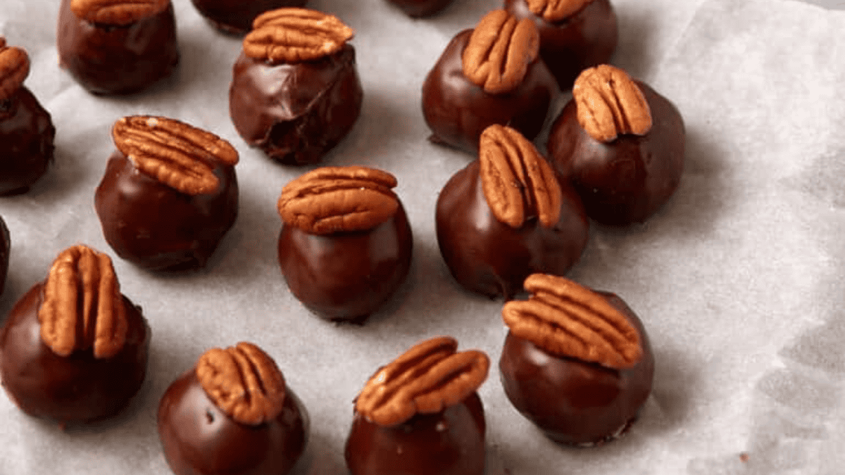 Rows of round chocolate truffles topped with pecan halves are arranged on parchment paper. With their glossy coating and decorative pecans, these treats make irresistible Super Bowl desserts for any celebration.