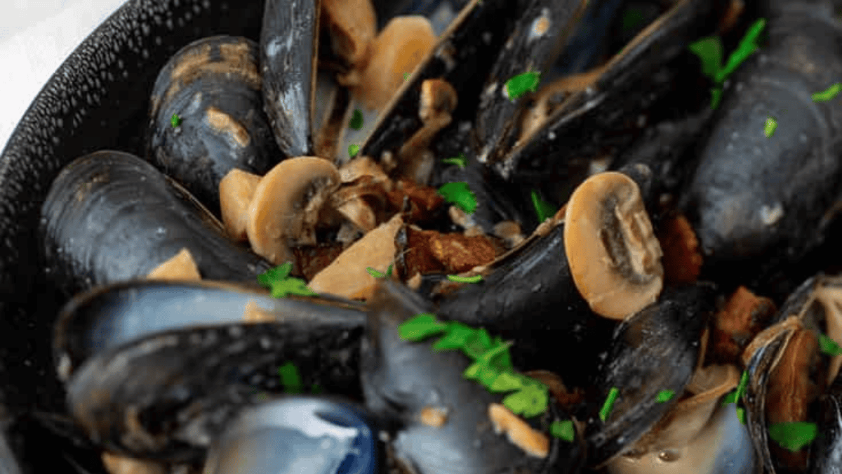 Close-up of a dish featuring cooked mussels in their shells, garnished with sliced mushrooms and fresh chopped parsley—an elegant option perfect for effortless weeknight dinners.