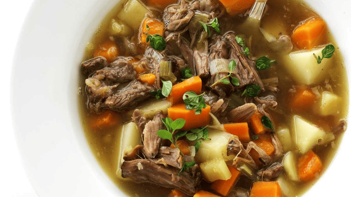 A bowl of beef stew with chunks of tender beef, potatoes, carrots, celery, and fresh herbs in a clear broth—a comforting classic from old fashioned dinner recipes.