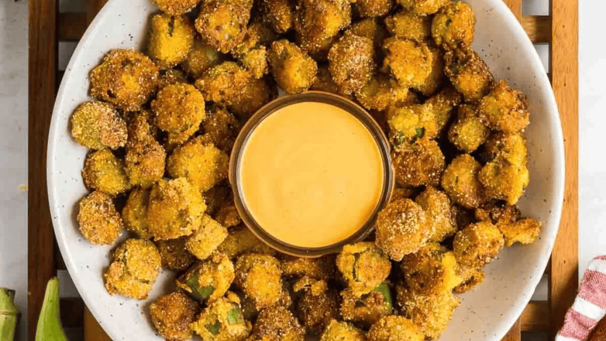 A white plate filled with crispy, golden fried pickles—a classic among southern snacks—arranged around a small bowl of creamy dipping sauce.