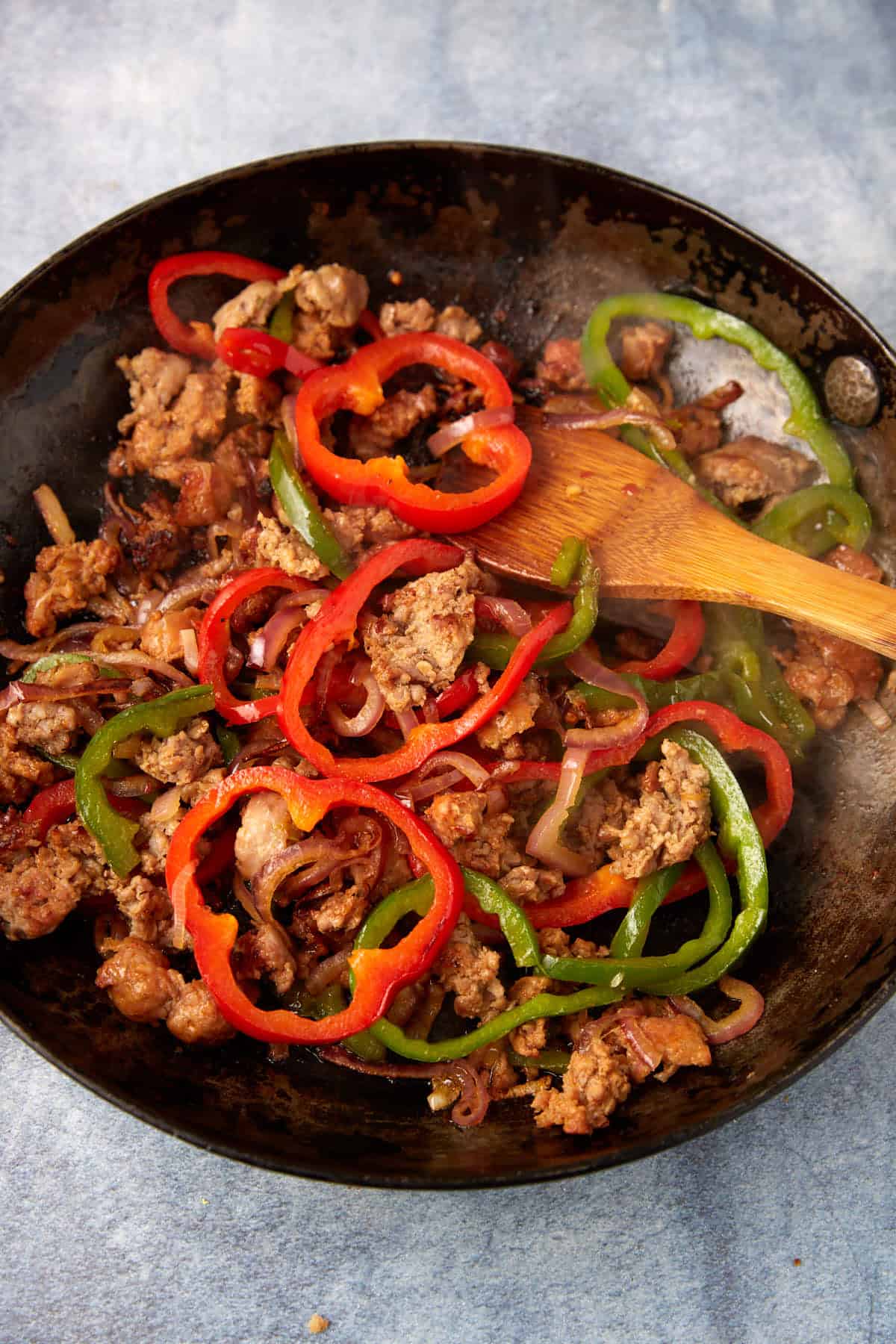Sausage with peppers and onions added in a skillet.