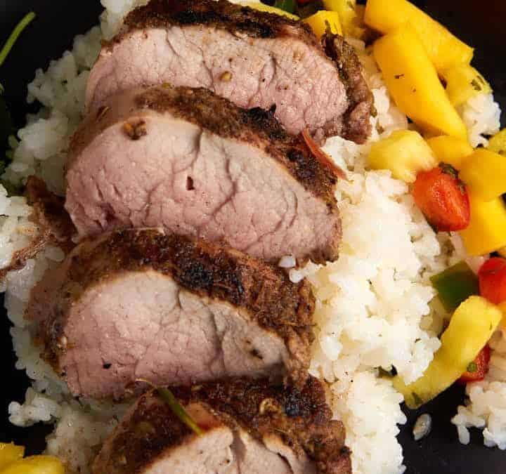 A plate of sliced pork tenderloin on rice with pineapple salsa.