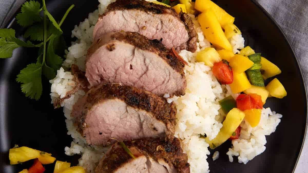 A plate of sliced pork tenderloin on rice with pineapple salsa.
