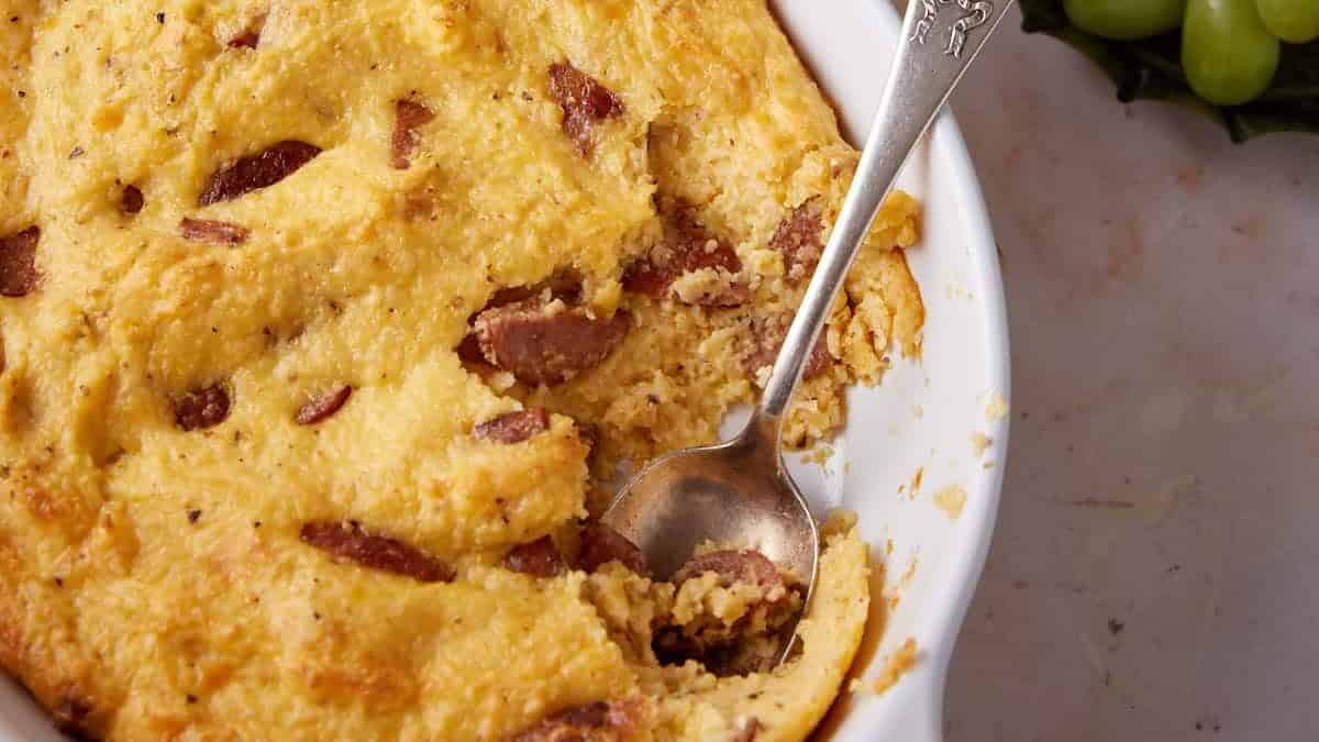 A deep baking dish packed with cheesy grits and browned sausage, set with baked eggs.