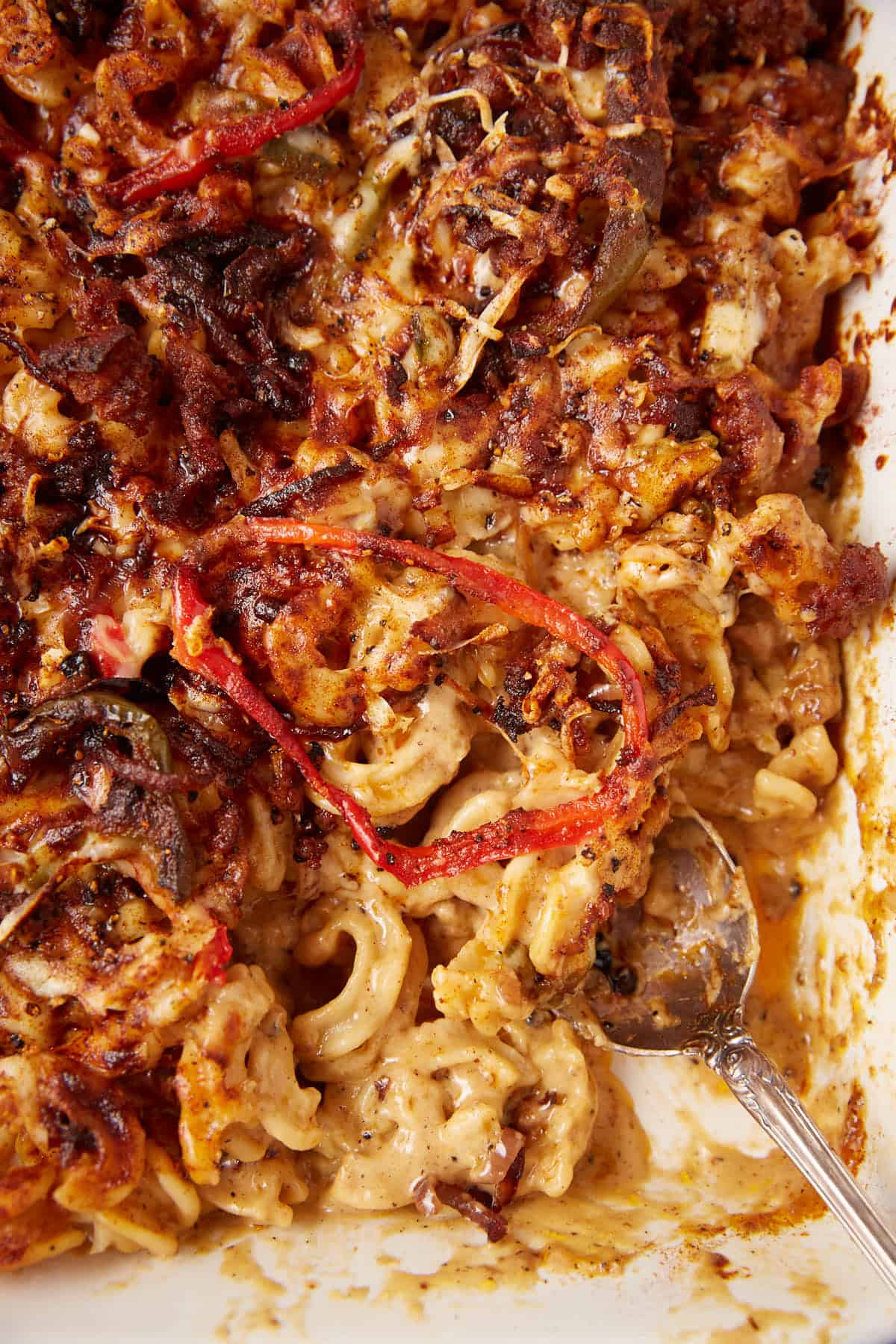 A serving spoon in a baking dish of sausage mac and cheese.