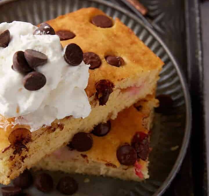 Two chocolate chip pancakes with whipped cream on top.