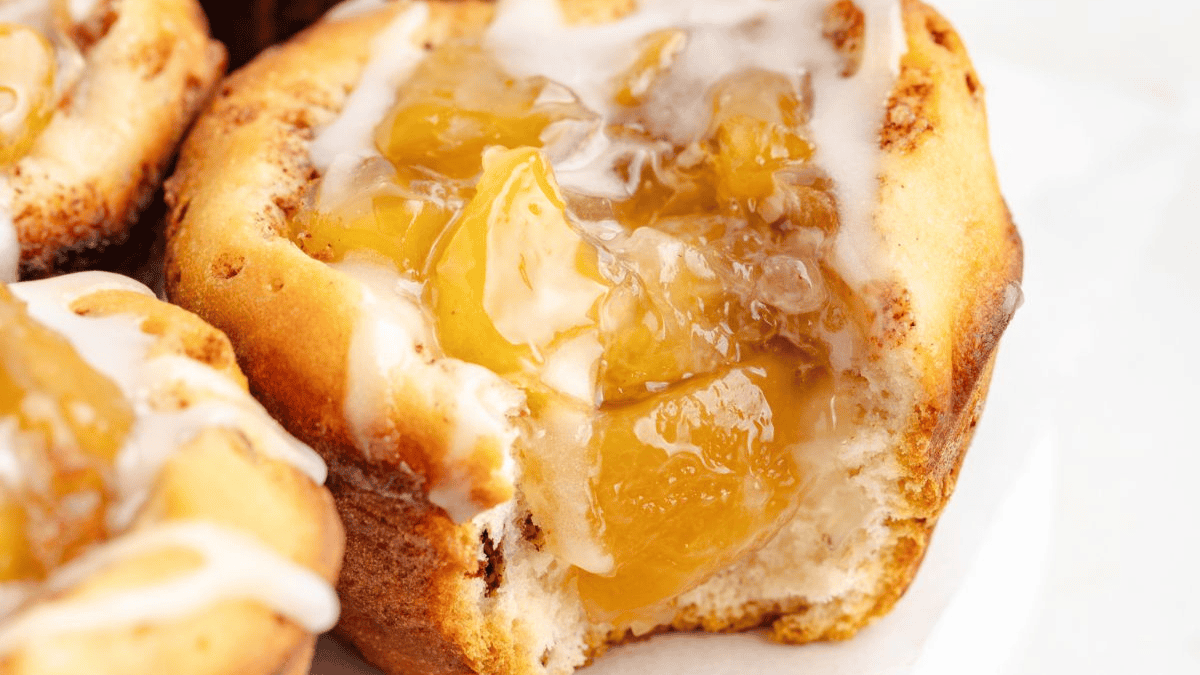 A close-up of a sweet pastry filled with glossy apple pie filling and drizzled with white icing. Perfect for fans of quick dessert recipes, the golden-brown pastry is soft and fluffy, with a bite revealing its delicious inside.