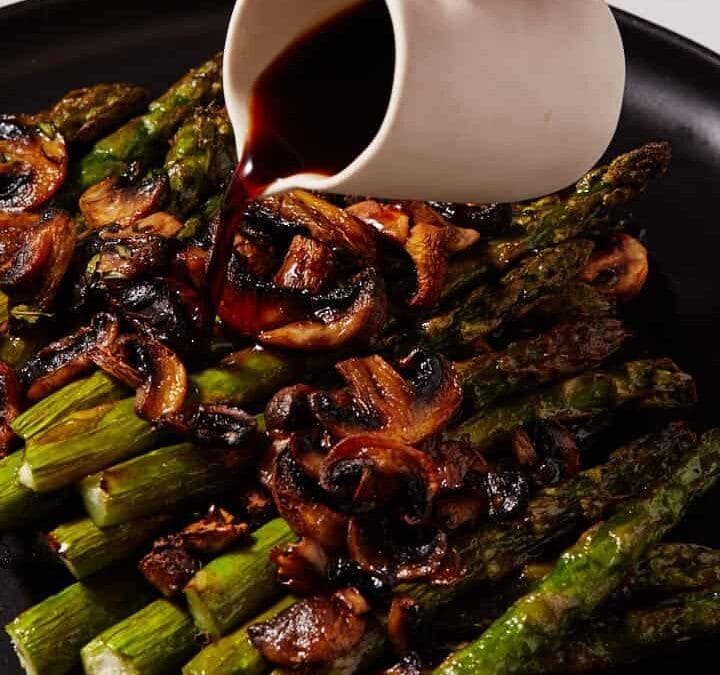Balsamic vinegar being poured over asparagus and mushrooms.