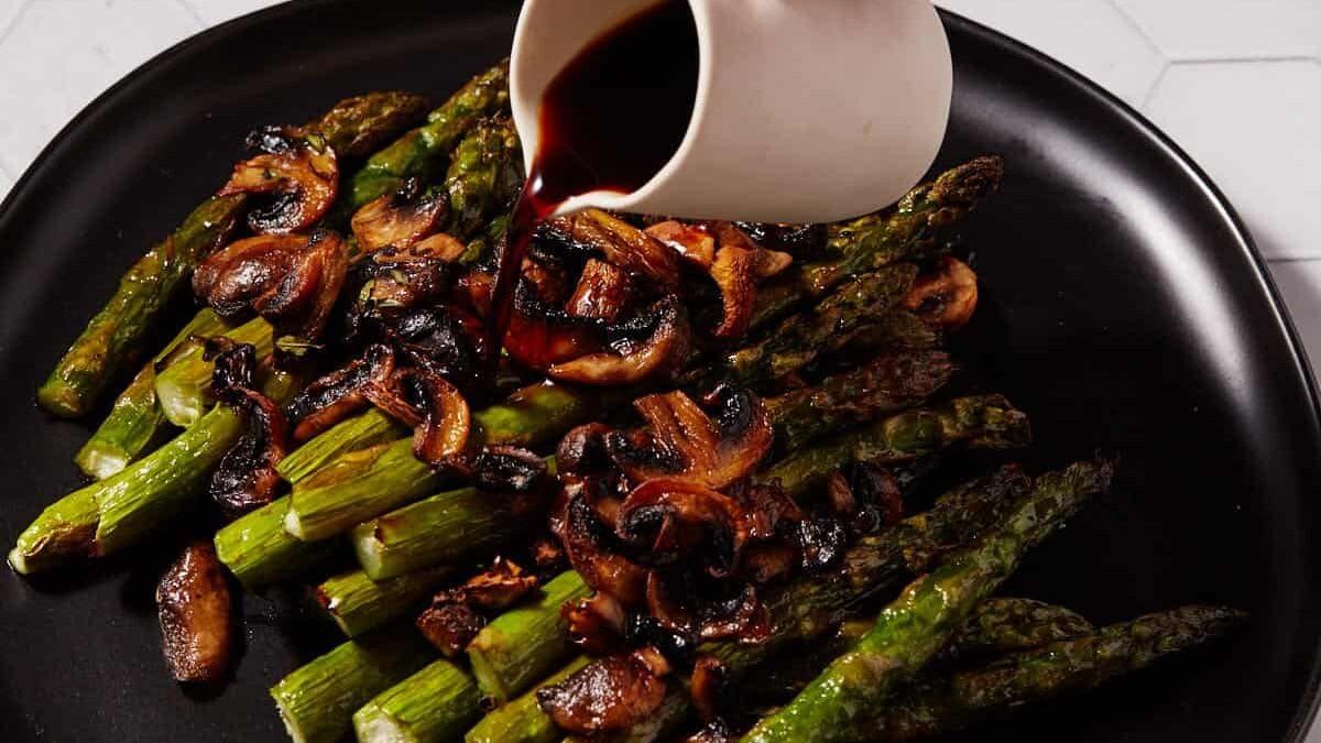 Balsamic vinegar being poured over asparagus and mushrooms.