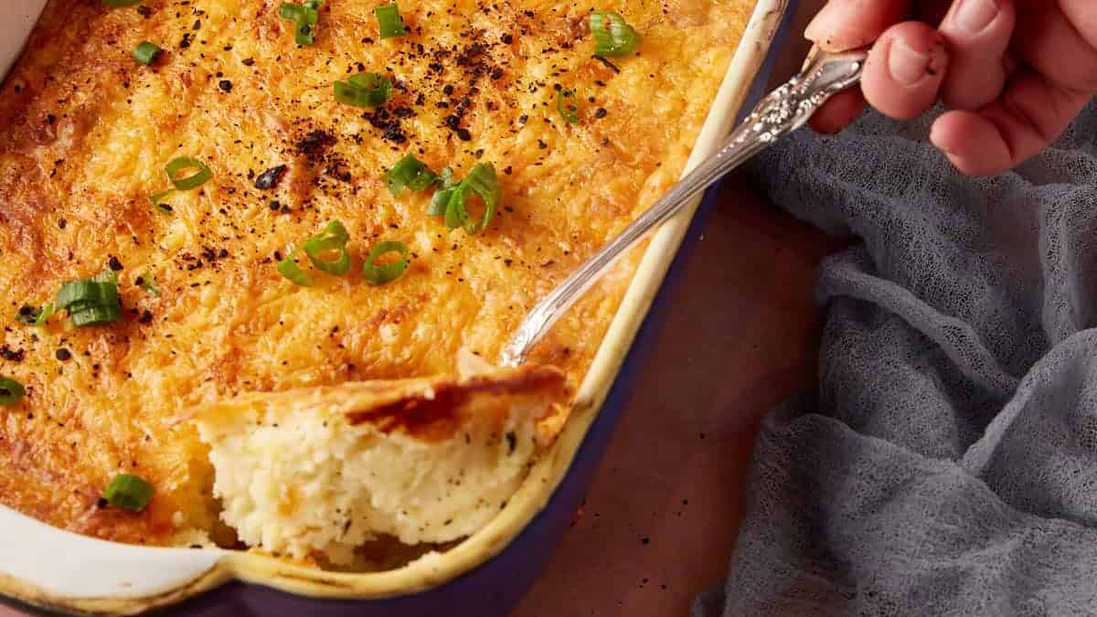 A serving of baked mashed potatoes being taken out of a casserole dish.