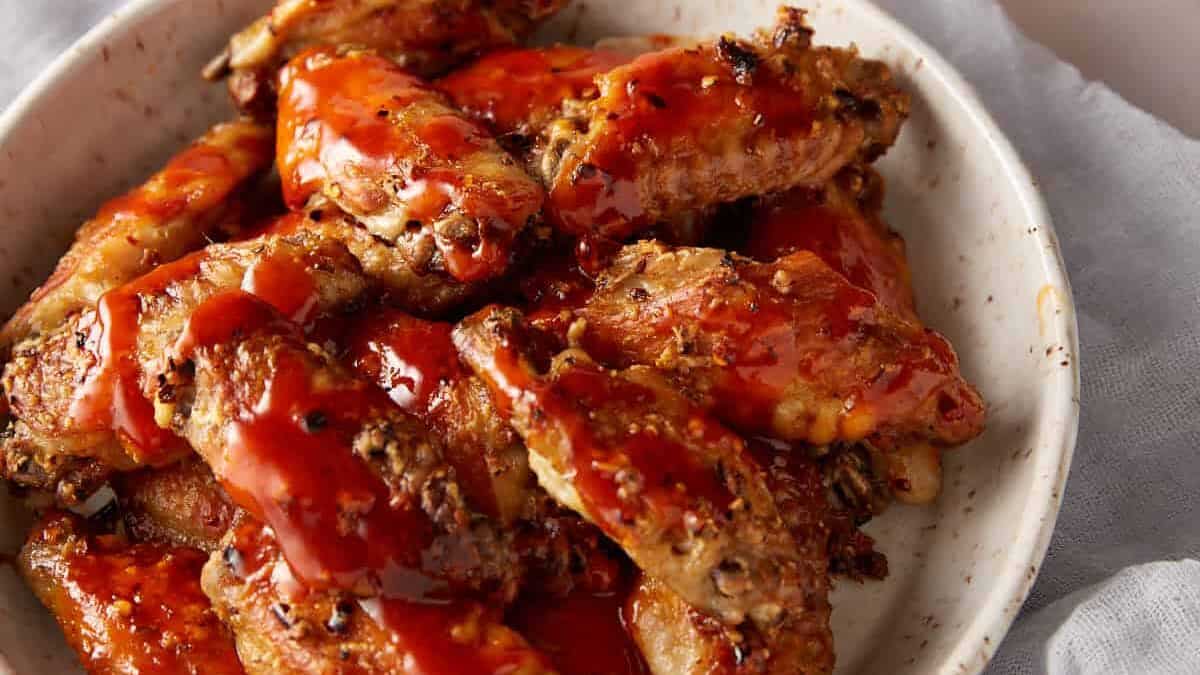 Buffalo chicken wings on a platter next to a pitcher of sauce.