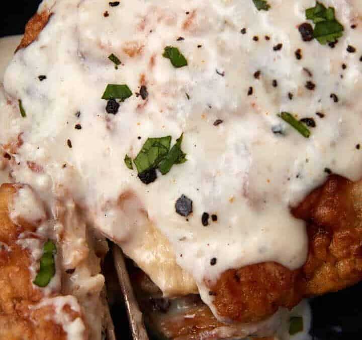 chicken fried chicken with gravy on a black plate being cut into with a fork.