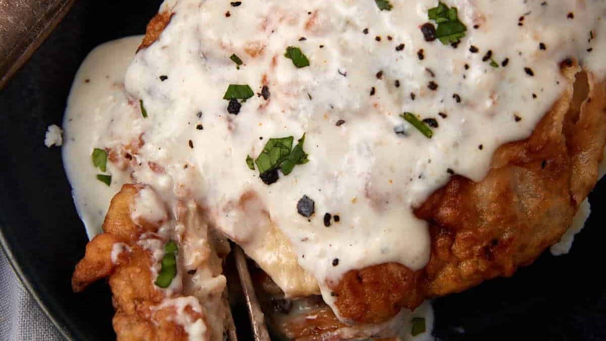 chicken fried chicken with gravy on a black plate being cut into with a fork.