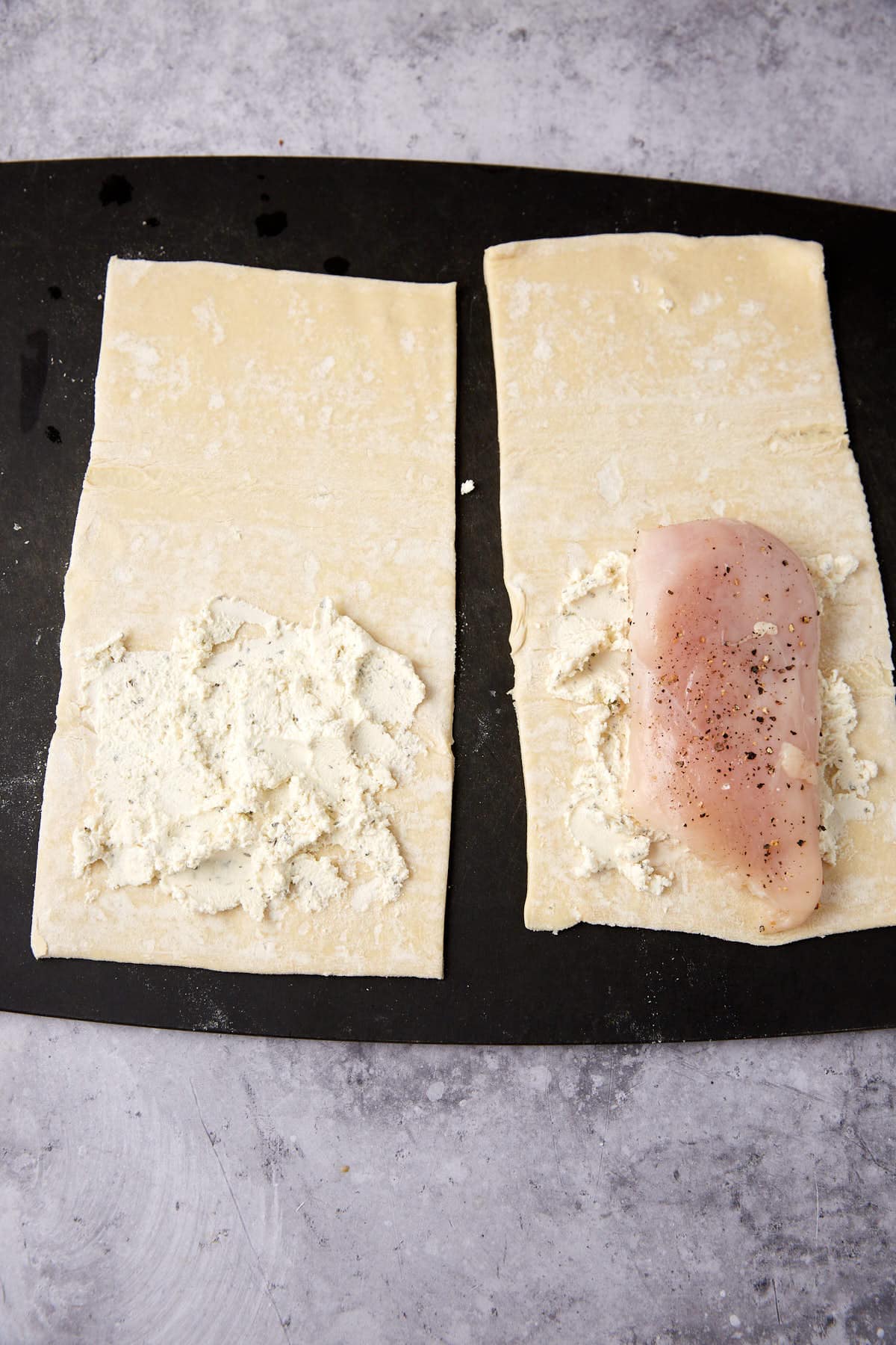 puff pastry sheets cut in half with garlic herb cheese on the bottom halves, one with a chicken breast.