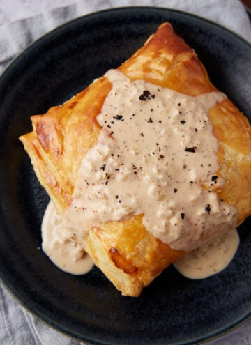 chicken in puff pastry covered in mustard cream sauce on a black plate.