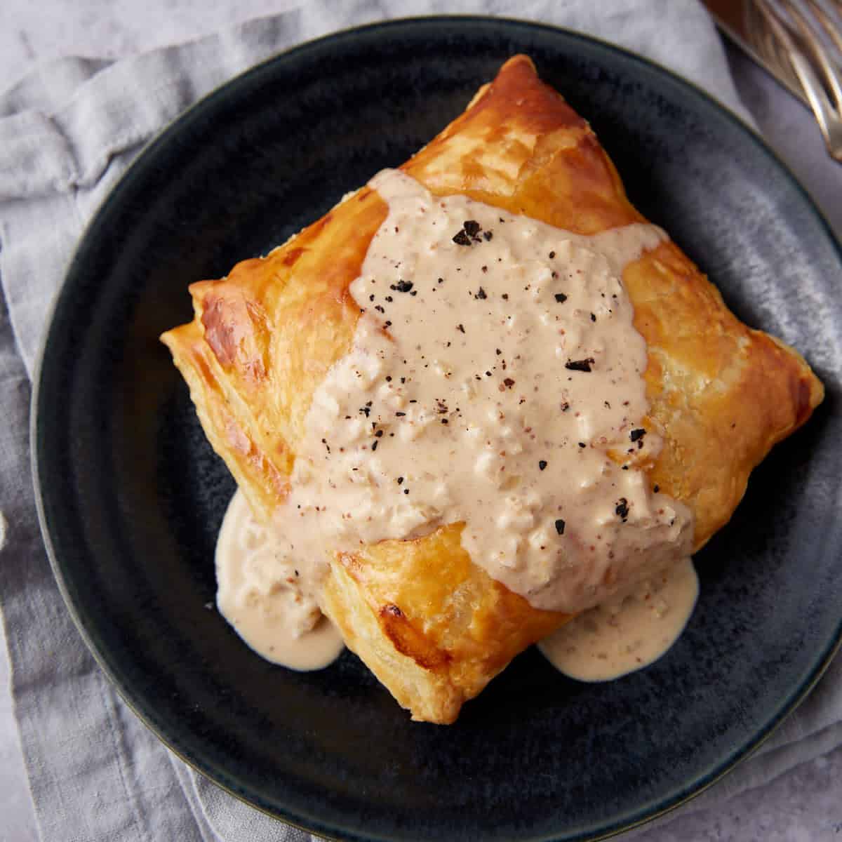 chicken in puff pastry covered in mustard cream sauce on a black plate.