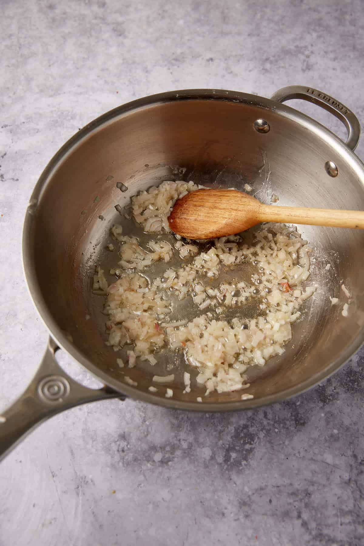 shallots being cooked in a saucepan with butter and wooden spoon.