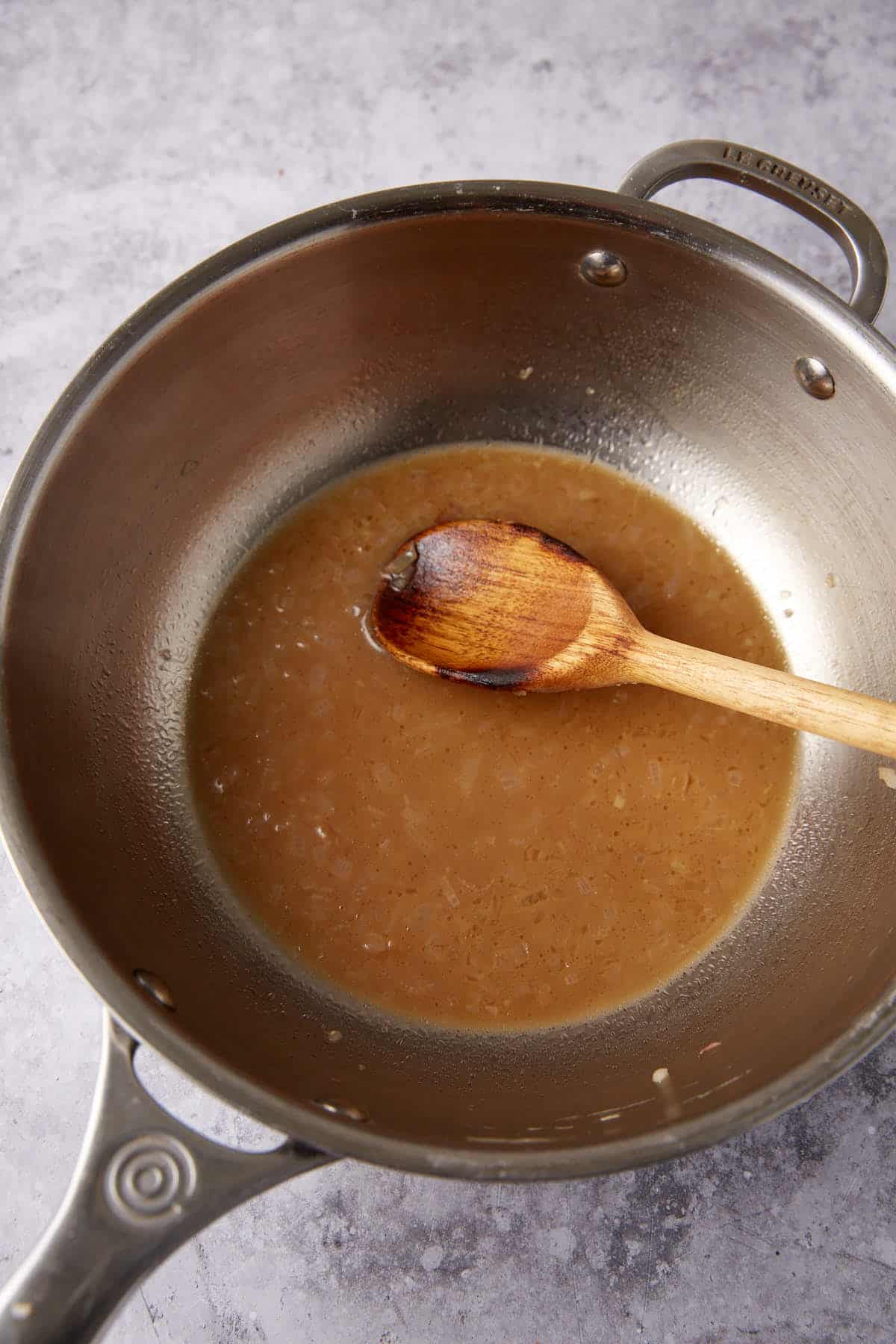 chicken broth and shallots in a saucepan with a wooden spoon.