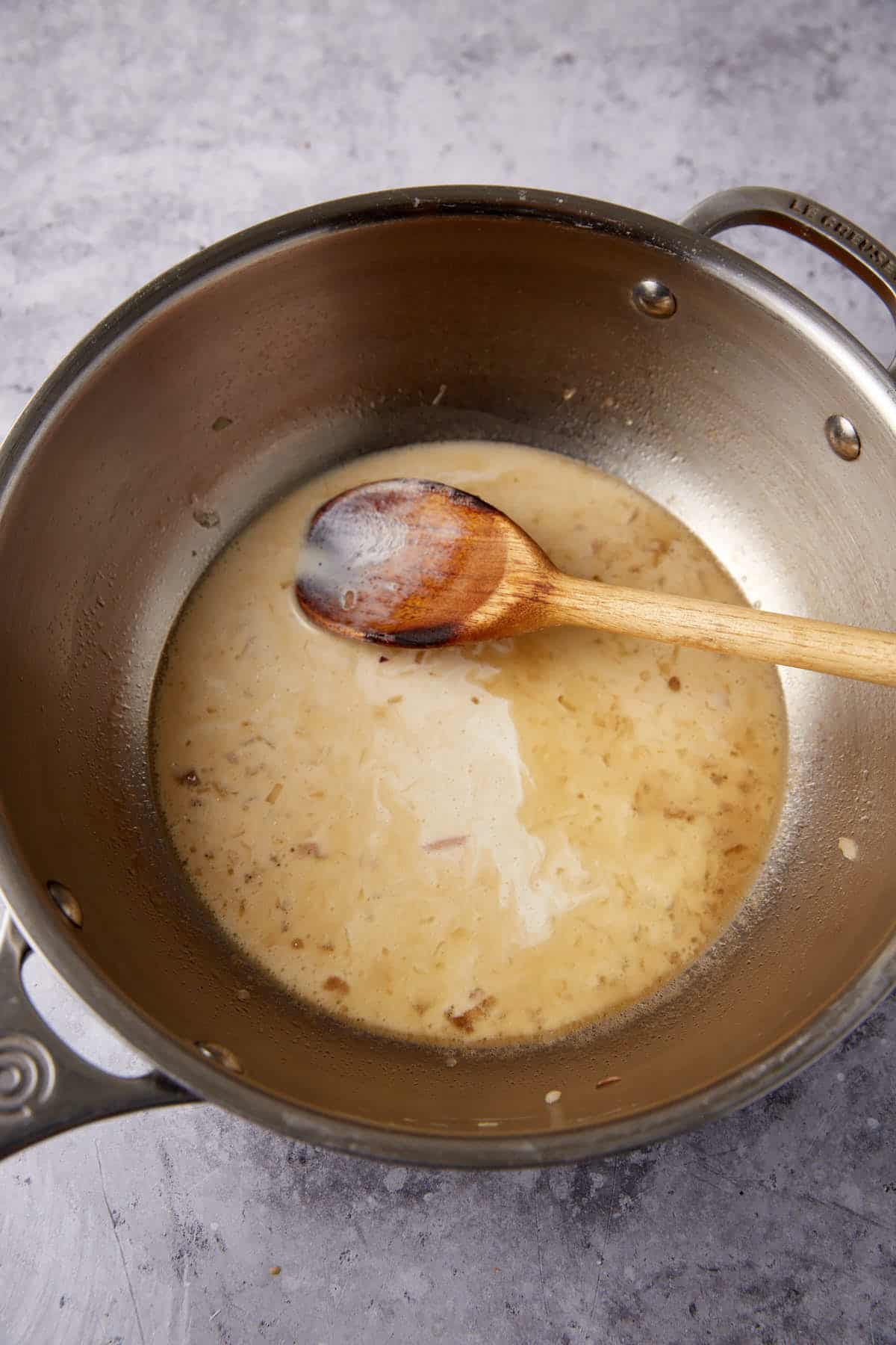 heavy cream added to the sauce in a saucepan with a wooden spoon.