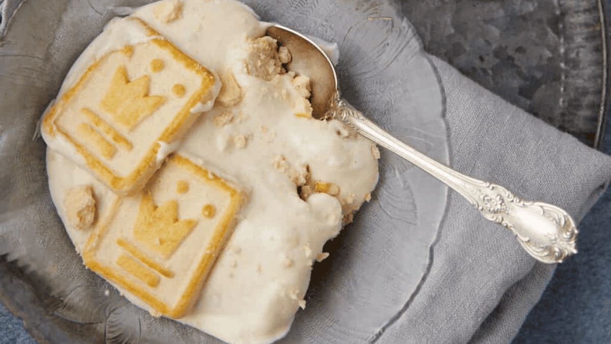 A classic old school dessert topped with two rectangular biscuits featuring a crown design, served on a plate with a silver spoon resting beside it on a folded gray napkin.