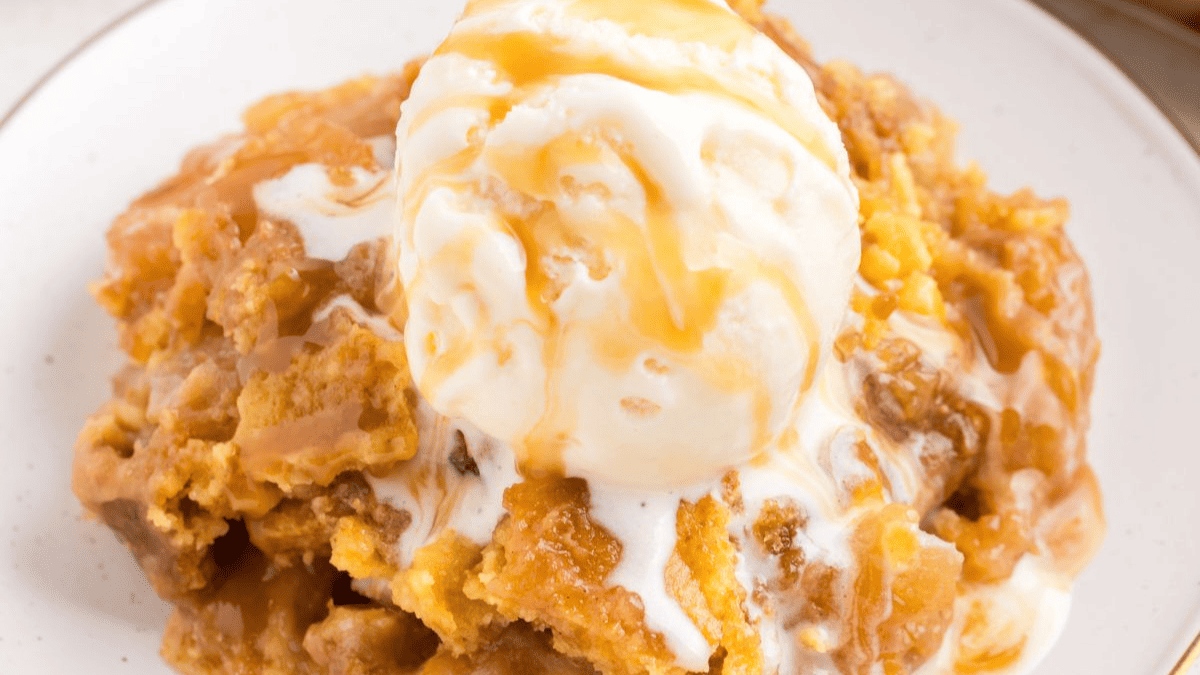 A close-up of a dessert featuring a scoop of vanilla ice cream topped with caramel sauce, served over a warm, golden brown apple cobbler—perfect for fans of classic apple desserts.