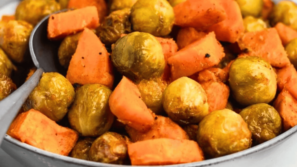 A close-up of roasted Brussels sprouts and sweet potatoes, lightly seasoned, served in a bowl with a serving spoon—an inviting option for Easter side dishes.
