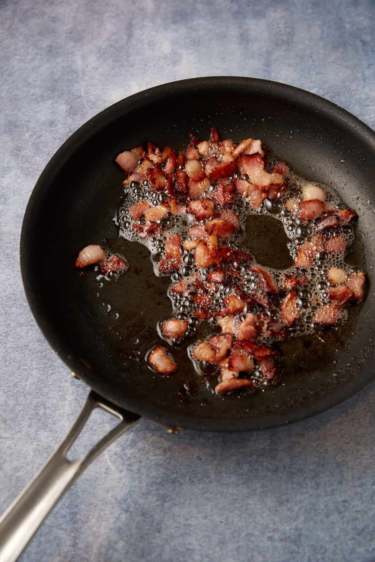 bacon being cooked in a skillet on a gray background.