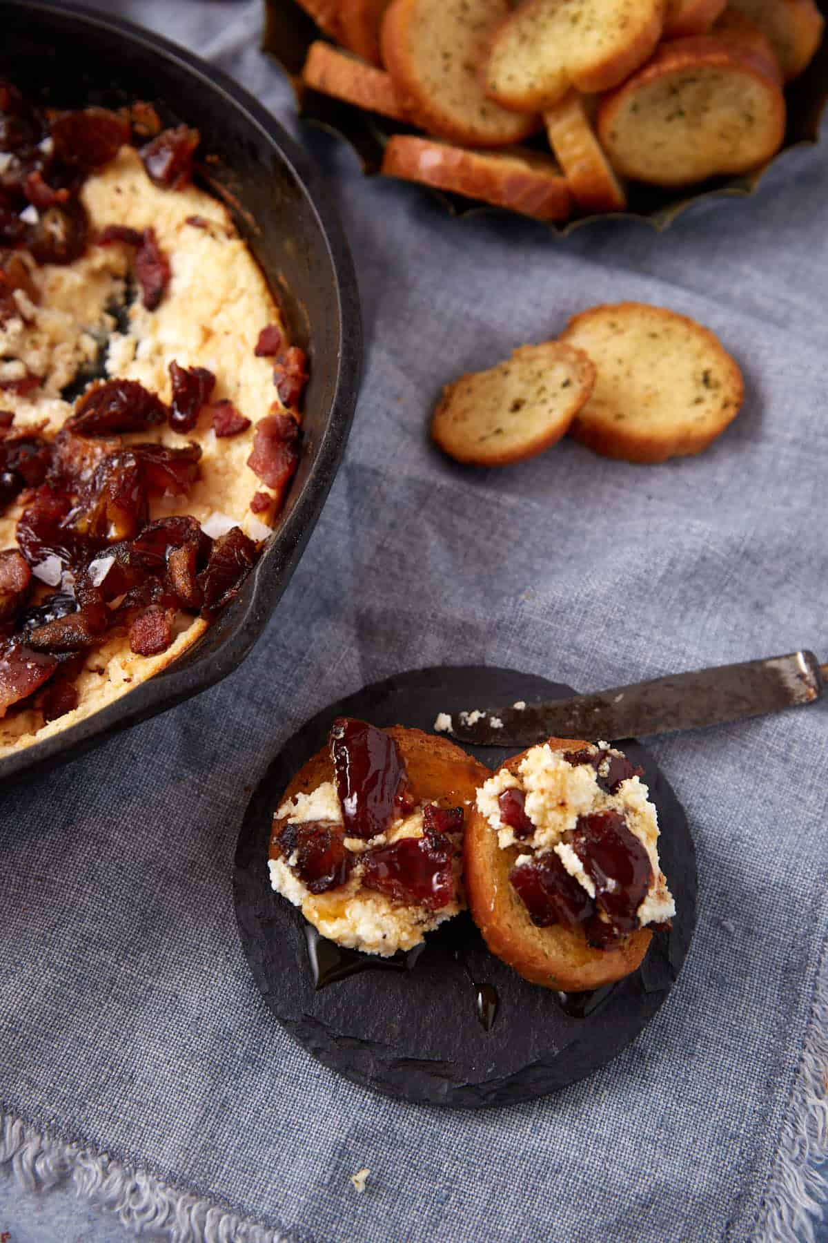 gray background with goat cheese dip off to the side with two small pieces of bread covered in goat cheese dip.