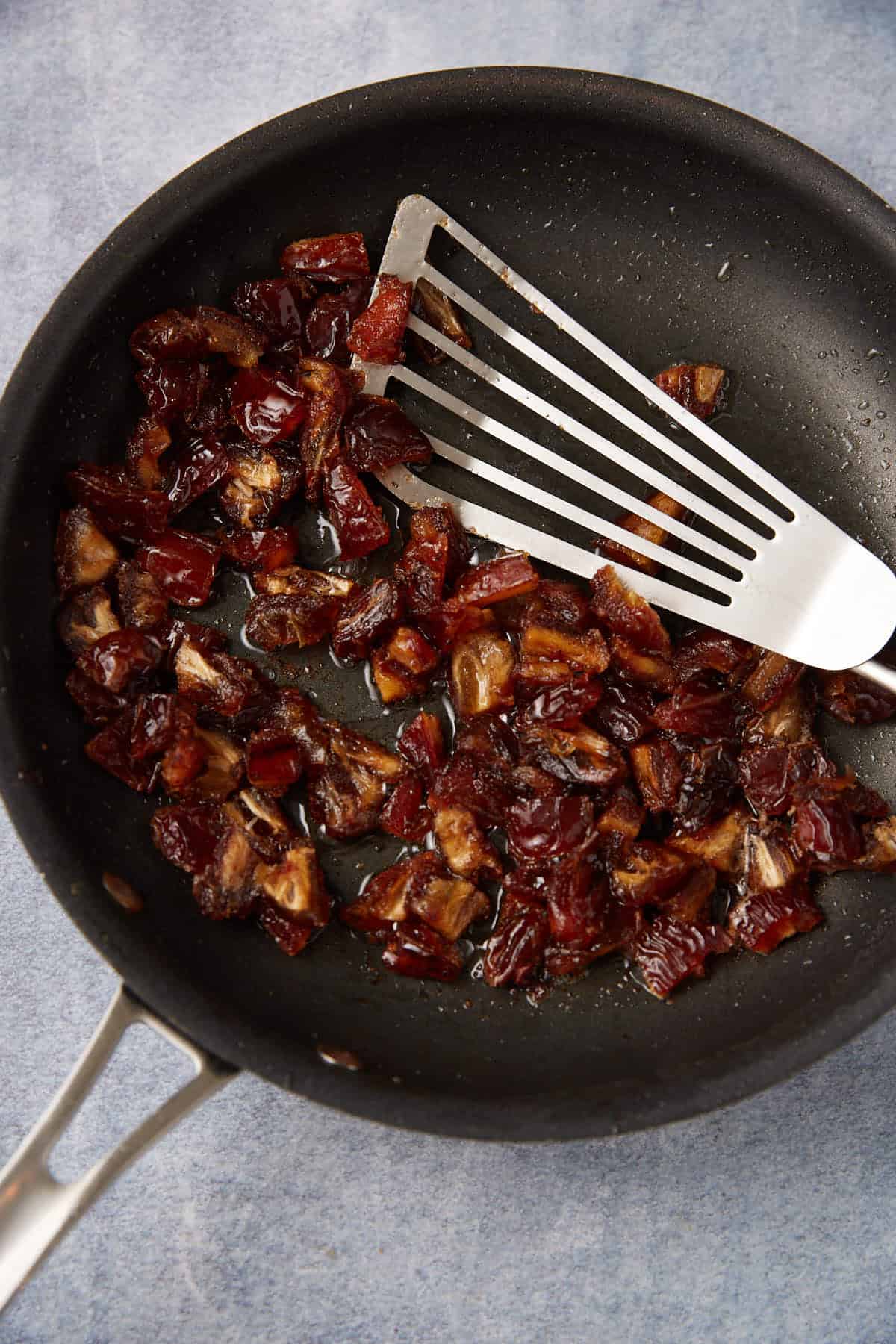 chopped dates soaking in leftover bacon grease with a metal spatula.