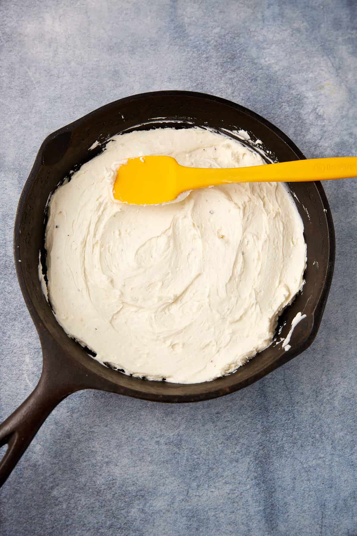 cream cheese mixture being spread into a cast iron skillet with a yellow spatula.