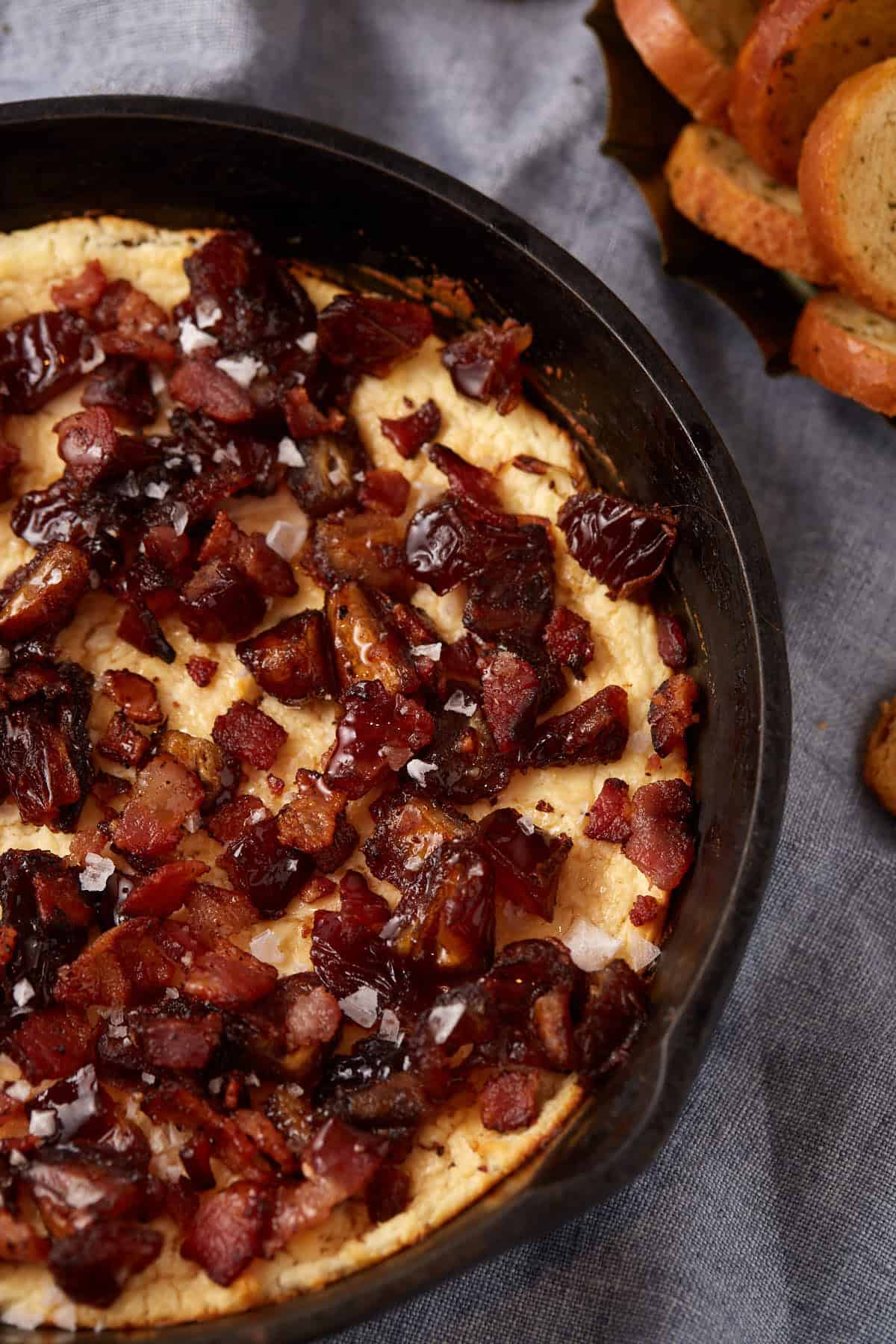 close up of goat cheese dip with dates, bacon, and hot honey in a cast iron skillet.