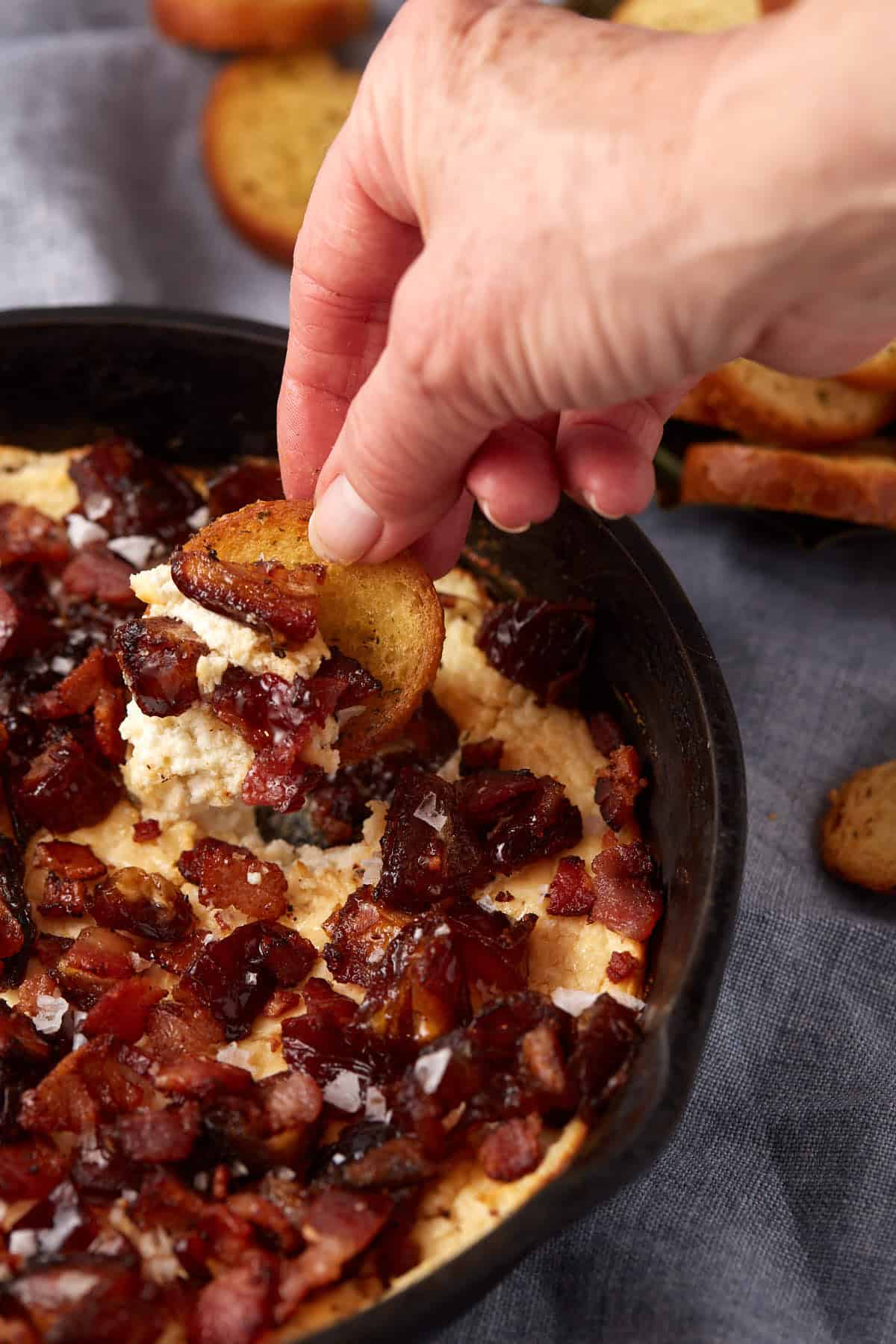 hand with bread slice dipping into goat cheese dip.