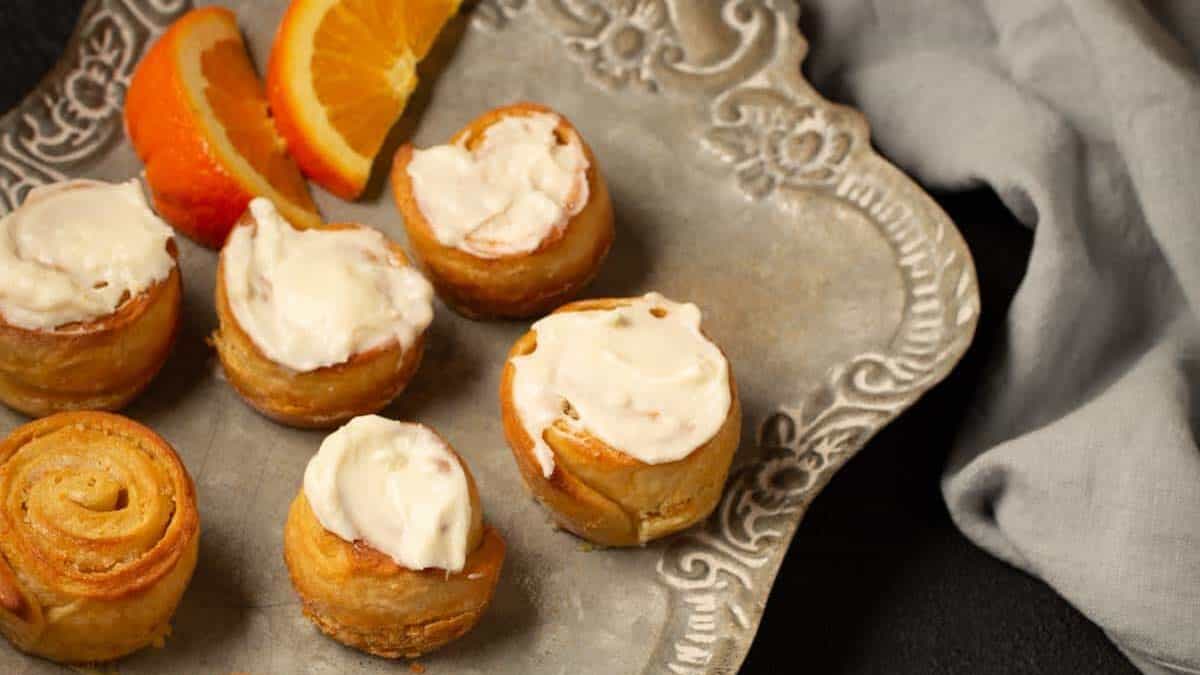 A platter of orange rolls half with frosting and half without.