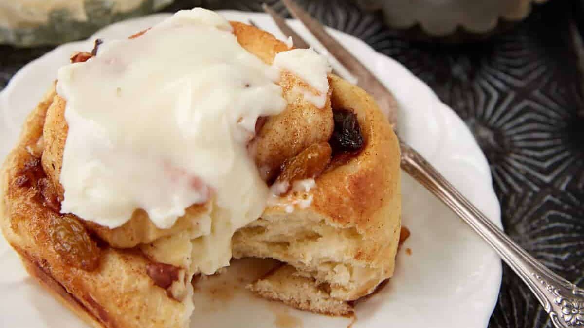 A frosted Hawaiian cinnamon roll on a plate with a fork.