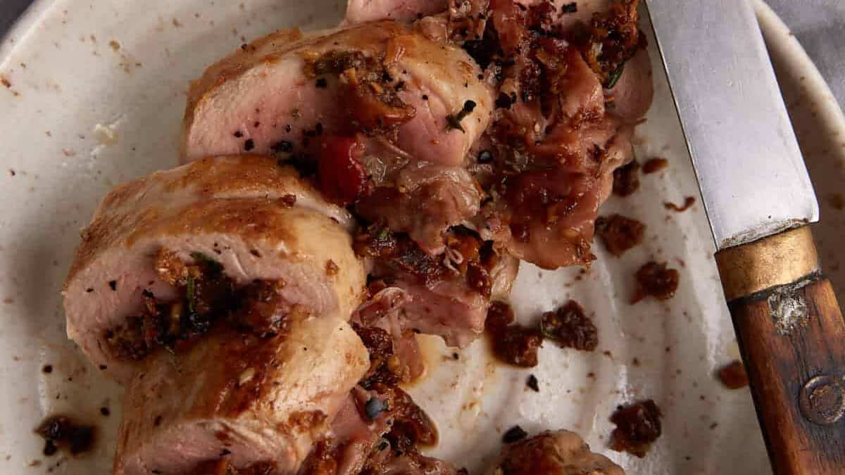 A platter of sliced pork tenderloin with a knife.
