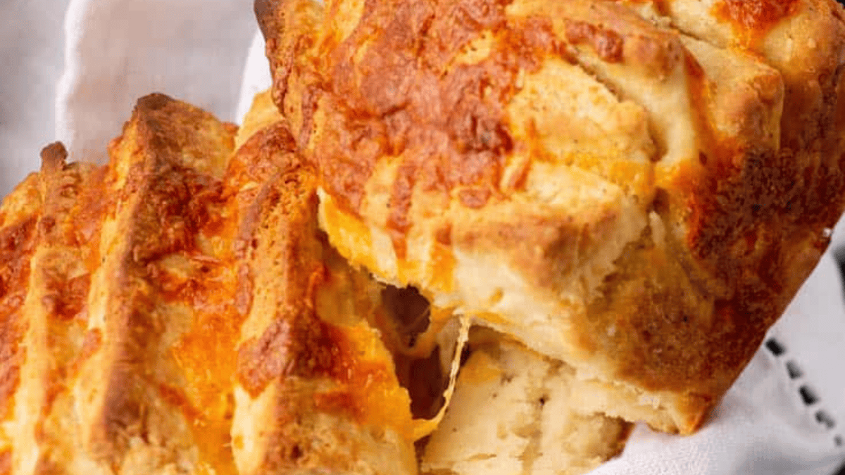 Golden, fluffy cheddar biscuits with crispy edges and melted cheese inside, these bites are a must-try for fans of classic bread recipes, stacked closely on a white cloth.
