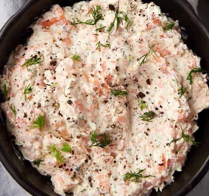 A bowl of cream cheese salmon dip next to a bowl of crostini.